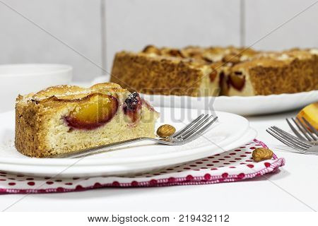 Homemade pie with almond frangipane and organic plums on white plate. Light background. Selective focus.