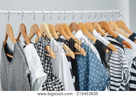 Stylish clothes hanging on wardrobe stand against light background