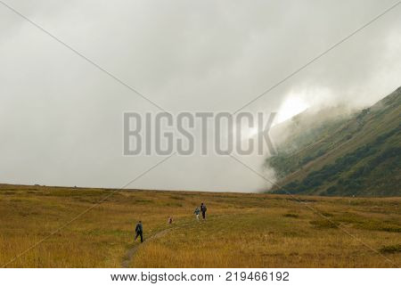 RUSSIA KRASNODAR KRAI - SEPTEMBER 23 2017: tourists walk on a mountain plateau in Caucasus Nature Reserve admiring the cloud rising from behind the pass