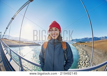 Cheerful woman wearing in red cup walks on the brige in Jokulsarlon Ice Lagoon, Iceland