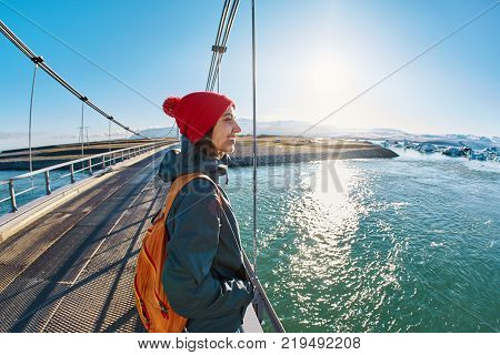 Cheerful woman wearing in red cup walks on the brige in Jokulsarlon Ice Lagoon, Iceland