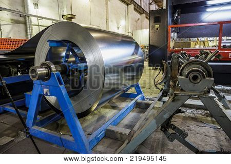 Roll of steel sheet and machinery tools for manufacturing metal pipes and tubes for industrial ventilation systems in the factory workshop, toned