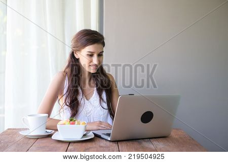 Woman having coffee and working outside. Working on laptop during her vacation in a tropical hotel. 