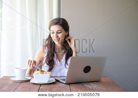 Woman having coffee and working outside. Working on laptop during her vacation in a tropical hotel. 