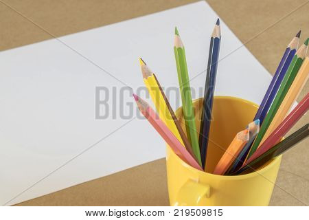 A lots of colour pencil in yellow cup and white paper on background prepare drawing