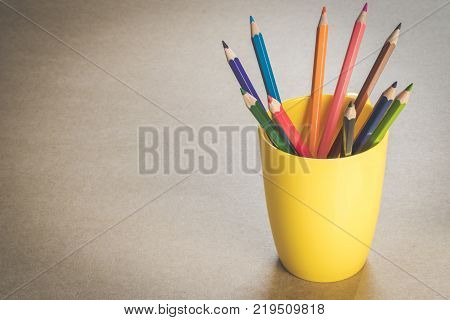 A lots of colour pencils in yellow cup on wooden texture paper.
