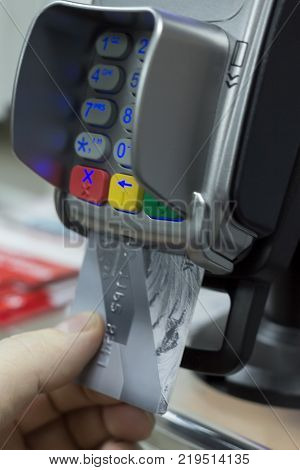 Close up of hand using credit card swiping machine to pay. Hand with credit card swipe through terminal for payment in cafeteria. Man entering credit card code in swipe machine.