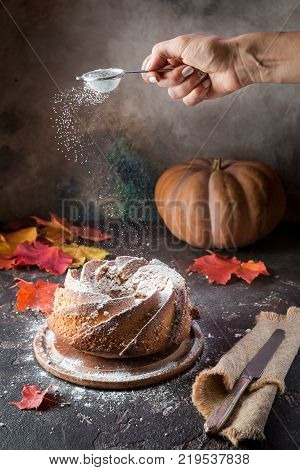 Bundt cake with saffron and rum covered with white glaze on rustic background with autumn decorations