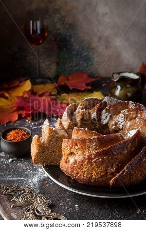 Bundt cake with saffron and rum covered with white glaze on rustic background with autumn decorations