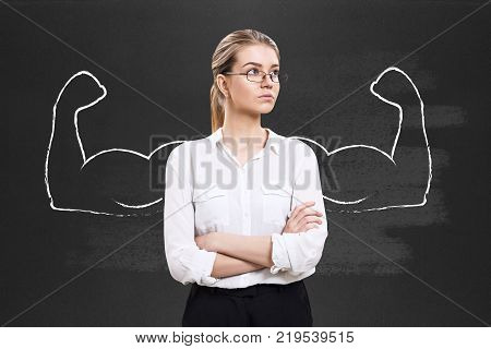 Business woman stands over chalkboard with drawn powerful hands.