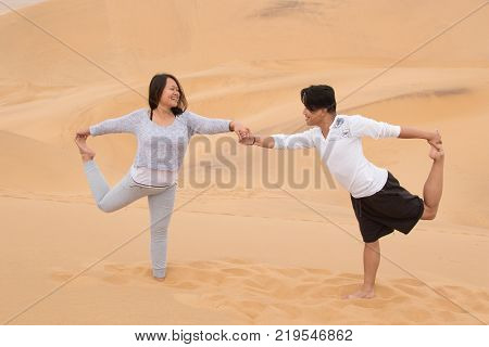 An Indonesian girl and Filipino boy doing yoga exercises on Dune 7, the highest sand dune in the world, in Walvis Bay, Namibia