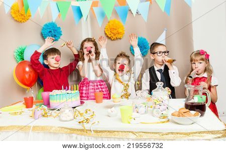Group of smiling children playing on the birthday party in decorated room. Happy kids blowing in pipes on birthday party