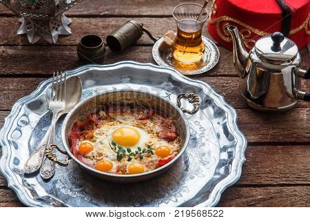 Traditional turkish breakfast with eggs and pastirma, with tea and metal dishware.