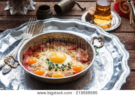 Traditional turkish breakfast with eggs and pastirma, with tea and metal dishware.