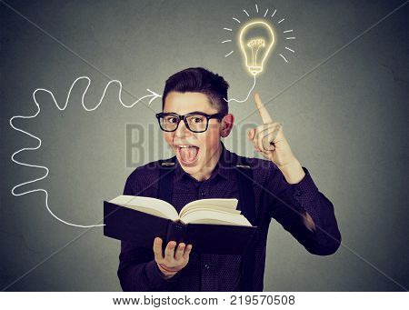 Amazed young man in glasses reading book comes up with an idea
