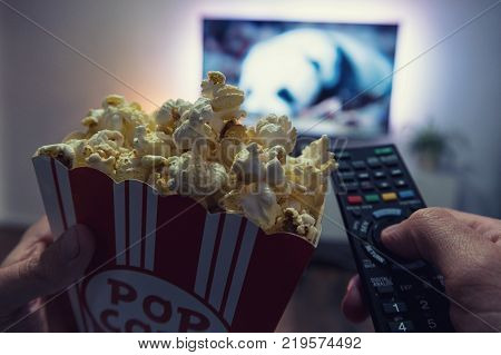 Pov shot from a young man watching a movie at home with popcorn and TV Remote control in his hands. ideal for websites and magazines layouts