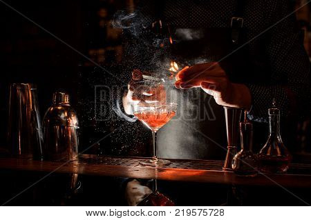 Bartender in black apron and blue shirt splitting pieces of ice by little piolet at a bar counter