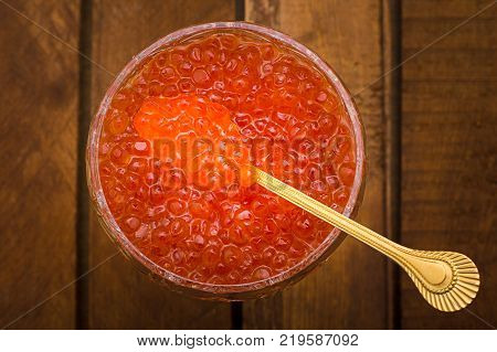 Red caviar in glass jar with gold spoon close up. Sea food. Healthy eating. Diet. Wooden rustic background. Top view. Selective focus