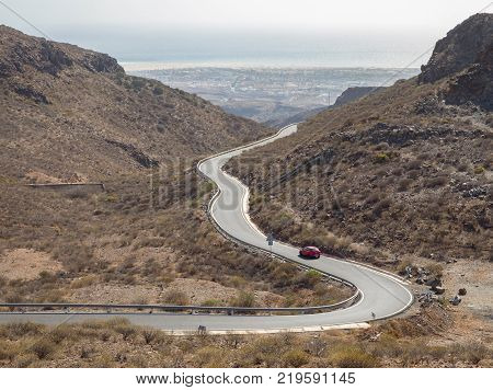 Curved winding road with a red car in the mountains in Gran Canaria