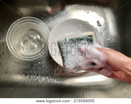 Right hand woman holding sponge washing dishes with bubble foam from washing powder on the sink. Concept cleaning.