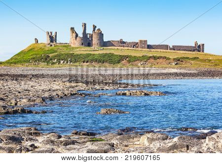 The coast of Northumberland in northern England between the villages of Craster and Embleton. Dunstanburgh Castle, a 14th-century fortification, can be seen in the background.
