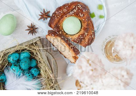 Traditional Greek Easter bread - tsoureki sliced in Easter decorations with painted blue quail eggs in the nest and flowers. Easter Festival concept.