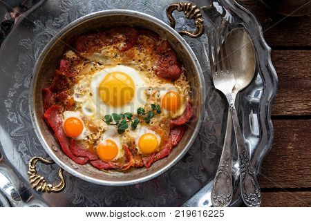 Closeup of Turkish pastirmali and fried egg in a copper pan on wooden table.