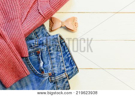 Womens casual clothing. Womens blue jeans, knitted pink sweater, hairpin on a wooden background with copy space for text. Top view