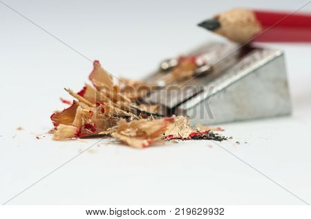 Sharp red pencil, sharpener, focus on the waste isolated on white background.