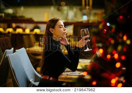 Winter holidays celebration concept. Girl with long hair celebrate new year and christmas. Festive fashion style decorations. Xmas party drinks toast alcohol. Woman enjoy wine in restaurant.