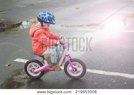 Happy child riding a bicycle in the fall. Cute little girl in safety helmet riding a bike outdoors. Little girl on a red bicycle.