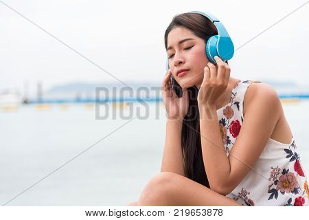Asian girls listen to classical music with the blue headphones at the beach, lonely with white summer dresses relaxing in the tropical sea.