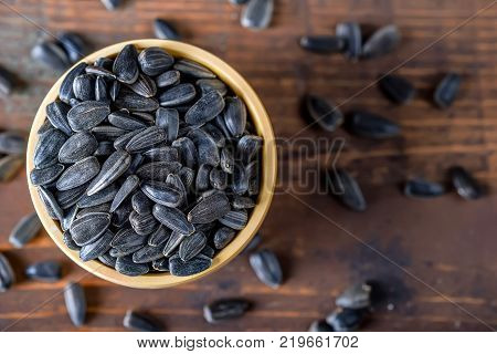 Close up unpeeled sunflower seeds in wooden bowl on dark wooden table
