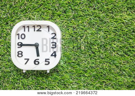 Closeup white clock for decorate show a quarter to six o'clock or 5:45 p.m. on green artificial grass floor in the garden textured background with copy space