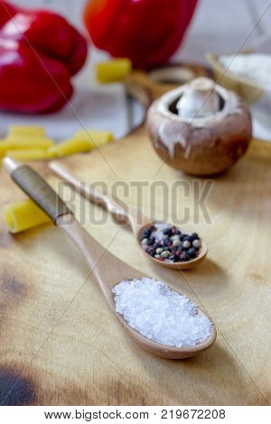 salt and pepper in wooden spoons surrounded by vegetales.