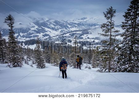 Two snowshoe hikers taking a break to enjoy a fantastic mountain view in the Swiss Alps. This is a breathtaking moment of pure serenity after a long hike nearby the 