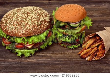 Large hamburgers with French fries for a quick snack on a dark table