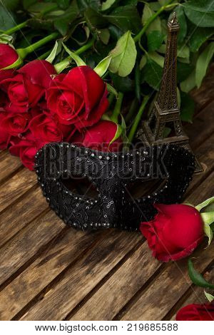 red fresh roses with black masque on wooden table