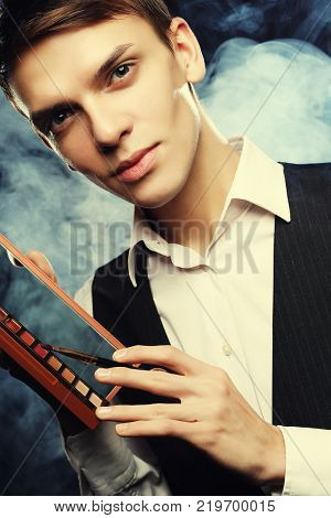 Male make-up artist  staying on dark  background, holding profes