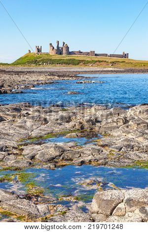 The coast of Northumberland, in northern England, between the villages of Craster and Embleton. Dunstanburgh Castle, a 14th-century fortification, can be seen in the background.