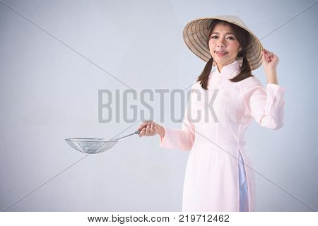 beautiful woman in pink dress and vietnam hat holding cooking utensils.