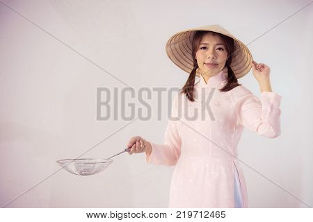 beautiful woman in pink dress and vietnam hat holding cooking utensils.