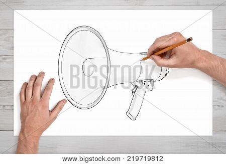 Two male hands in first person view draw a megaphone with a pencil on white paper. Public speaking. Speech preparation. Public relations job.
