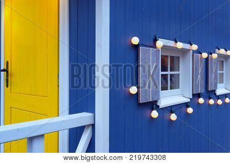 Windows with light bulbs on a blue painted wooden house wall with a yellow door