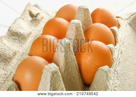 Raw brown chicken eggs in a cardboard tray with cells on sacking on a white wooden table. Ingredients for cooking