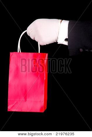 Formalne rękawiczce dłoń trzymająca czerwony Gift Bag na czarnym tle