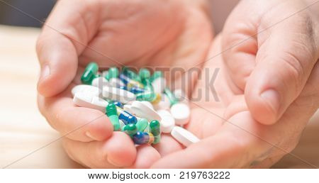 handful of different colored pills being held over wood background.