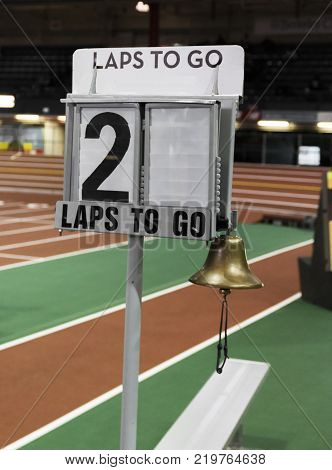 A lap counter with a bell to ring when there is one lap to go is set up next to the finish line to show runners how many laps they have to run in an indoor track and field arena.