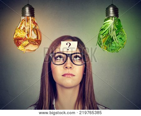 Woman in glasses question mark on head thinking looking at junk food and green vegetables light bulb isolated on gray background.