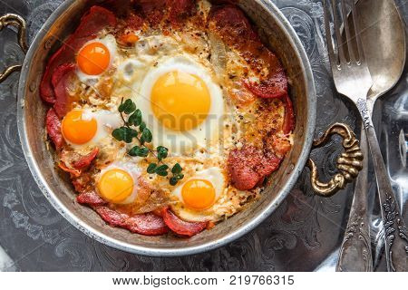 Closeup of Turkish pastirmali and fried egg in a copper pan on wooden table.